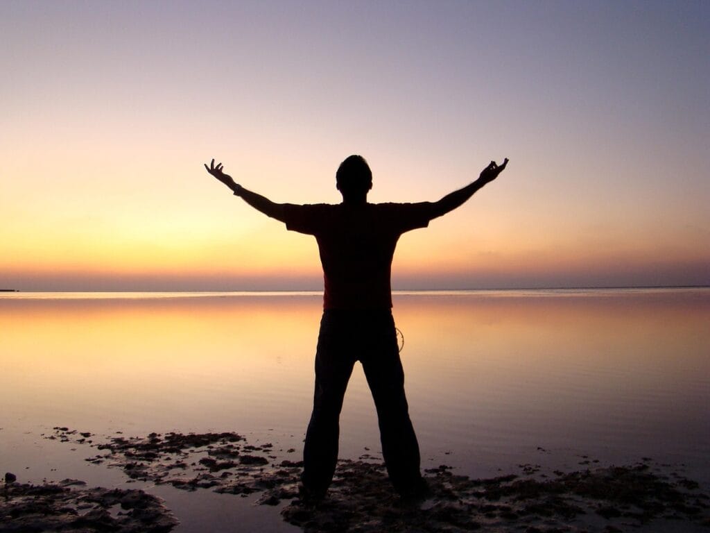 a man, filled with Self-Love, standing on a beach with his arms outstretched