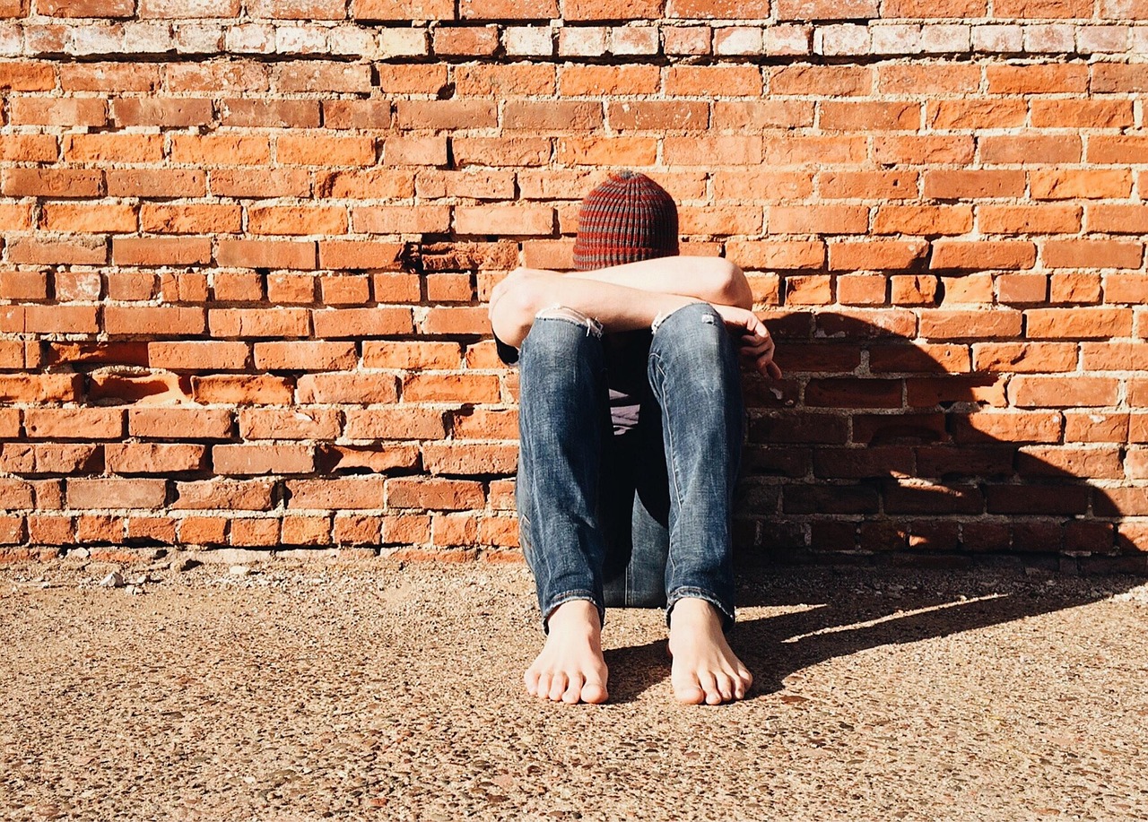 Person sitting againt a wall, facing down and experiencing schizophrenia.