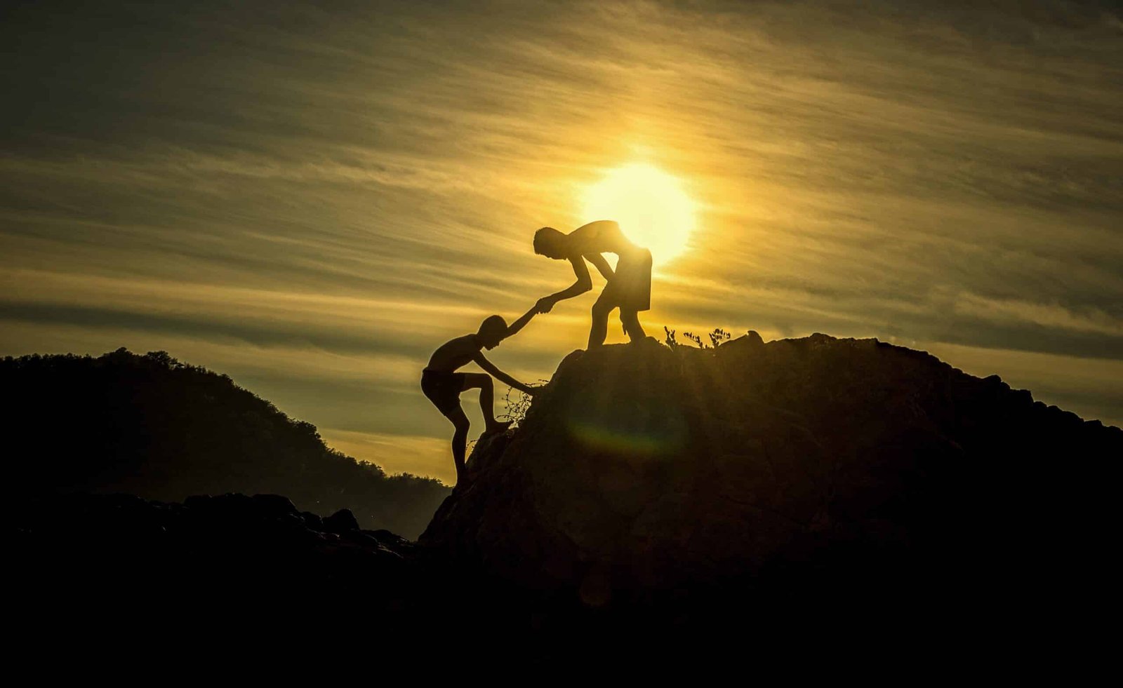 2 people climbing a mountain during sunset while staying positive in difficult times